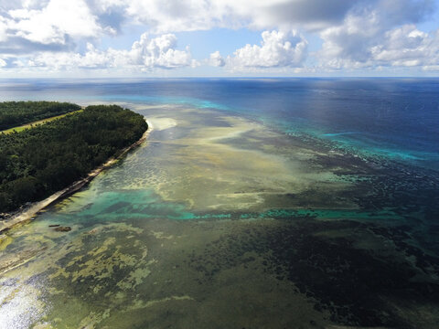 Aerial view of Poivre Atoll with lush green forests, shallow coral reefs, and turquoise ocean waters under a cloudy sky Seychelles.