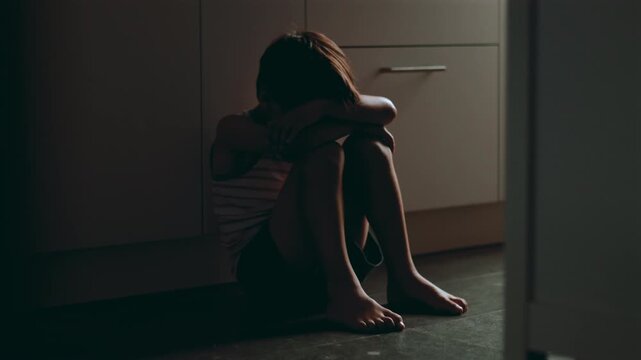 Child sitting alone on kitchen floor hugging knees and hiding face expressing deep loneliness depression and childhood trauma in quiet domestic space suggesting emotional neglect