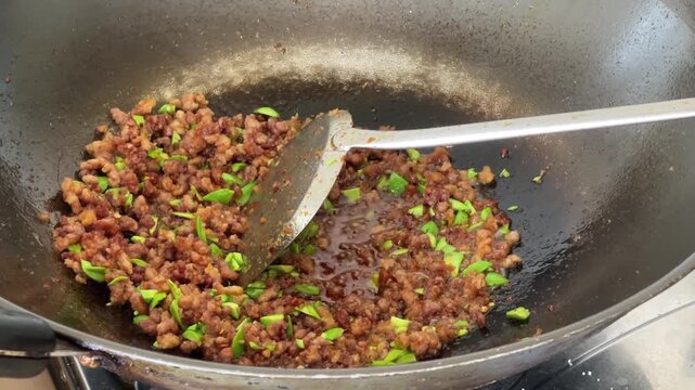 A close-up shows minced meat being stir fried with fresh petai Parkia speciosa beans in a hot wok, featuring sizzling oil and traditional cooking movements.