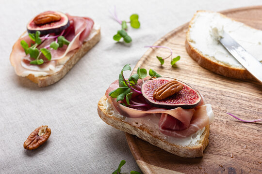 Slices of white bread with young cream cheese, meat, freshly sliced figs and radish sprouts.