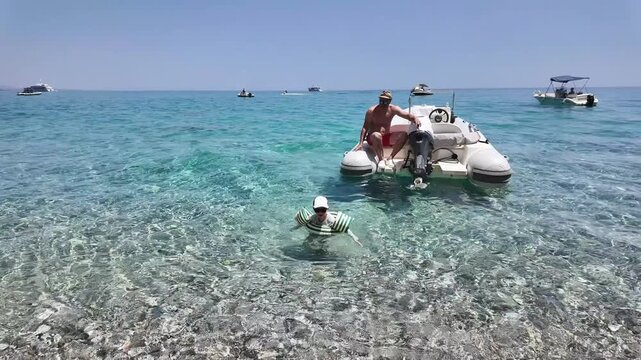 Kid in the sea with inflatable ring heading to the shore. Sunny coastal setting, transparent water, and relaxed summer lifestyle scene.