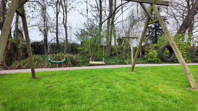 Static shot of an empty wooden swing set on a green lawn.
This horizontal video shows a quiet outdoor playground scene in the Flanders region. A sturdy wooden swing set stands on a well-k