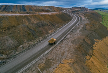 Aerial view shows large dump truck transporting materials on a wide dirt road at an open pit mine site during daytime © Evgenii Bakhchev