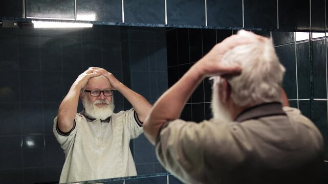 Elderly man stands in front of mirror. He ruffle turn his hairstyle into chaos