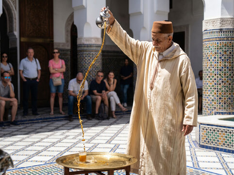 Moroccan man pours traditional mint tea into small glasses in a courtyard