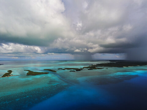 Aerial view of the Farquhar Group atolls with turquoise lagoons and coral reefs under dramatic storm clouds and rain showers in Seychelles.