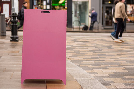 London street - Blank pink A-frame sign on busy city street pavement, space for copy