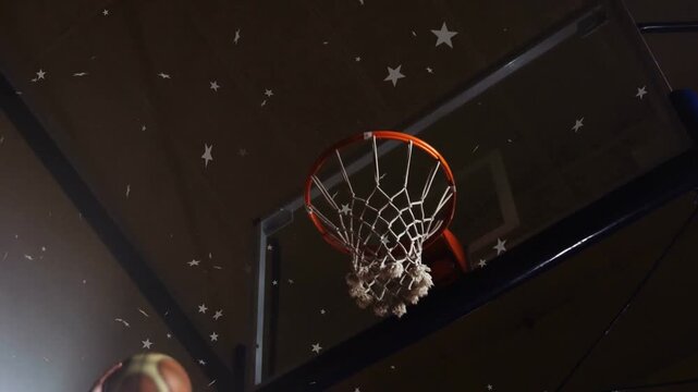 Player reaching arm releasing basketball in gym, ball passing rim, net settling under star overlay
