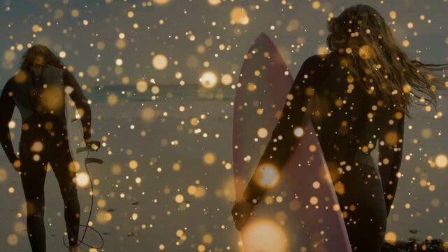 Surfing woman carrying pink board and man fixing leash, walking toward sea under gold bokeh overlay