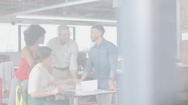 Four colleagues gathering at roundtable, fourth joining and handing sheet, reviewing design plans
