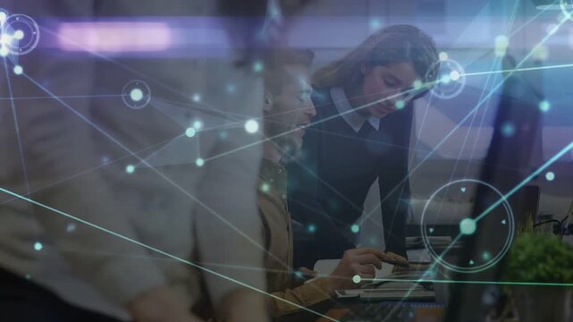 Standing coworker handing pages, seated shifting and reviewing, tech overlaying screen for business