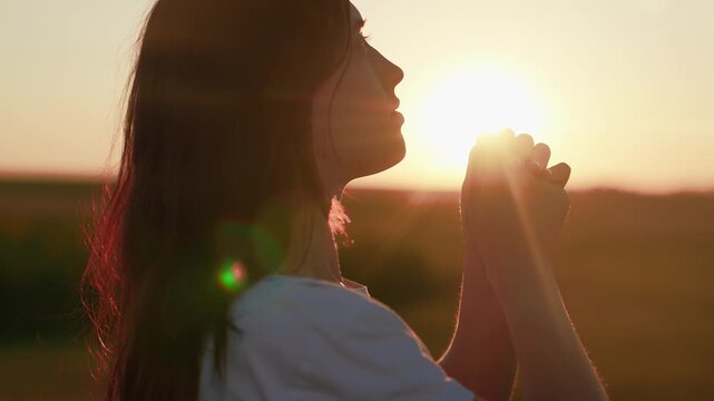 Young girl prays against sunny sky, caring for family children. Faith in God. Close-up Christian woman praying at sunrise. Relaxation meditation in nature. Apology. Hope. Life. Free man. Silhouette.