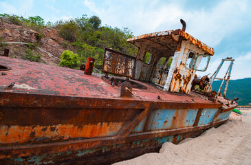 Fototapeta premium Rusted abandoned fishing boat stranded on sandy beach with decaying hull and corroded structure