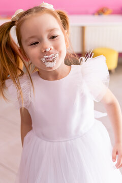 Little birthday girl with cake on face laughing at party