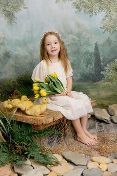 Cute child girl holding yellow tulips with ducklings, spring nature portrait with soft green background