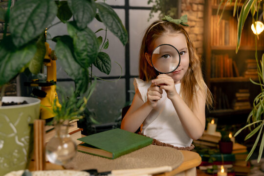 Child girl sitting at table looking through magnifying glass, looking at camera