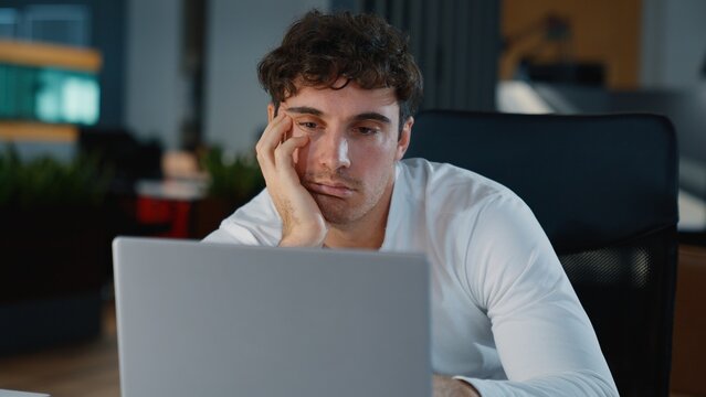 Overworked Caucasian tired business man working with laptop difficult job overload businessman male specialist guy professional fatigue work with computer monotone boring task in night evening office