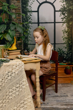 Little girl sitting at table and looking through magnifying glass, curious child exploring and learning at home