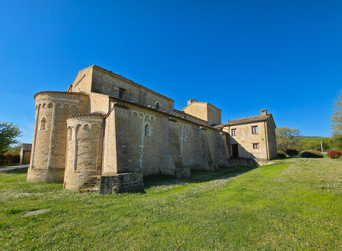 Exterior view of the Romanesque Sant'Urbano Abbey in Apiro with stone apses and green meadow, Marche region, Italy
