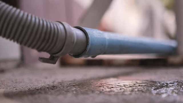 Close-up of water leaking from a hose connection with a visible droplet, showing a minor plumbing issue and water waste in a home setting.