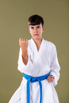 Karate student in white gi and blue belt performs a front stance with a closed fist, demonstrating focus and basic striking technique.