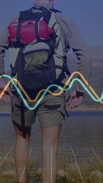 Vertical video: Cam revealing man hiking shore to lake, fixing pack as waveform grid showing route