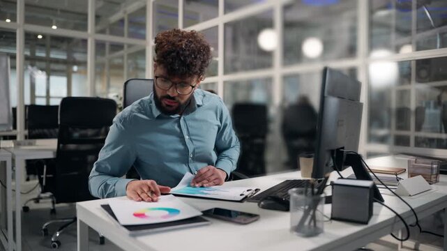 Busy Arabian business man analyzing colourful diagram paperwork writing notes finance managing ethnic businessman analyze sales trading datum male analysis documents write review stats guy at office