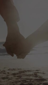 Vertical video: Senior couple walking beach showing linked hands shifting for travel with sun glare
