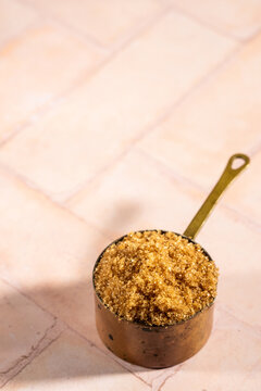 Brown sugar in a weathered copper measuring cup on a tile surface 