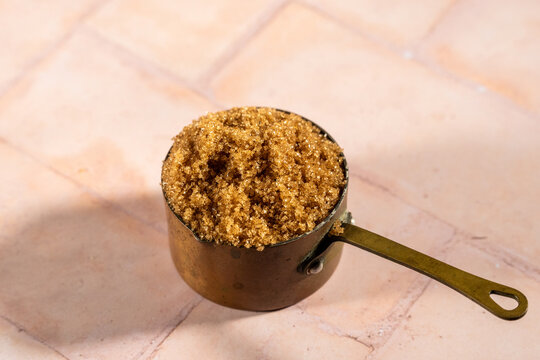 Brown sugar in a weathered copper measuring cup on a tile surface 