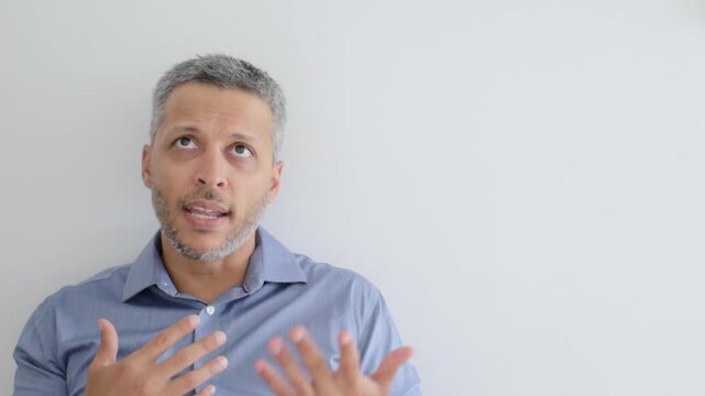 Confused mature man looking up and gesturing with hands against white wall