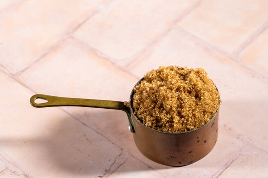 Brown sugar in a weathered copper measuring cup on a tile surface 