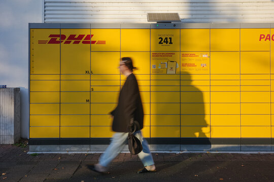 Dusseldorf, Germany - September 28 2025: DHL Packstation parcel lockers with pedestrian passing in front in motion blur effect