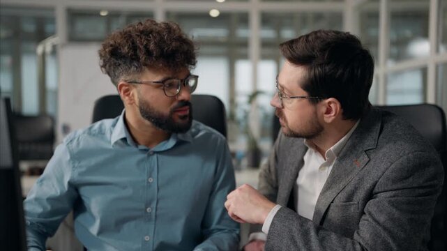 Two multiracial business men talking working computer in office partnership teamwork cooperation multiethnic businessmen males talk work Arabian intern communicate with Caucasian boss trainee mentor
