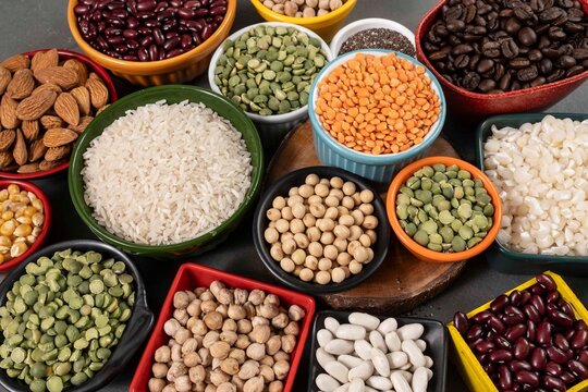 Assortment of healthy legumes, grains, and seeds in colorful ceramic bowls including rice, lentils, beans, chickpeas, and almonds, perfect for a balanced vegan and vegetarian diet and nutrition