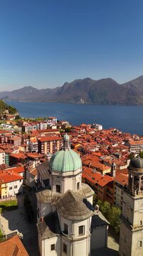 Drone aerial of Basilica di San Vittore in Verbania Intra, Lake Maggiore. Full church view with bell tower and weathered green copper domes above historic lakeside town.