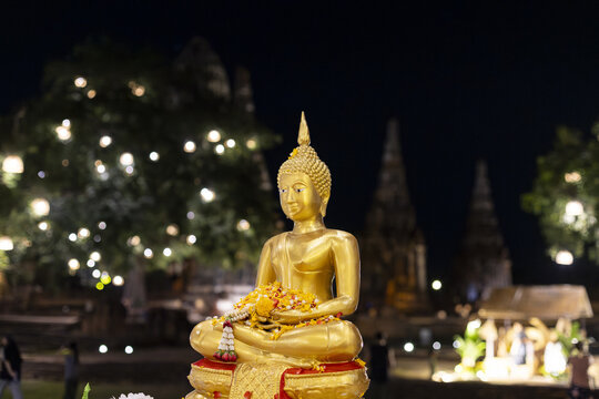 Golden Buddha statue sitting outdoor at night near ancient Wat temple ruin in Ayutthaya Thailand radiating peaceful serene emotion surrounded by glowing tree light under dark sky