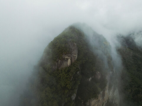 Aerial view of Morne Seychellois mountain peak with rocky cliffs and lush green forest partially covered by thick white clouds and mist in Port Glaud, Seychelles.