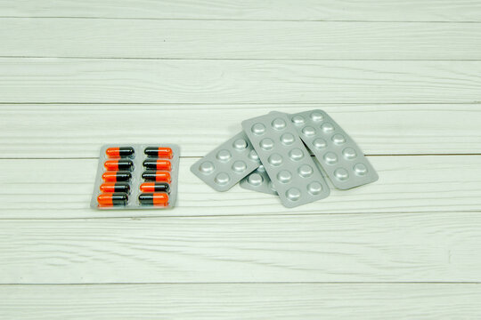 Blister packs with orange capsules and empty foil containers arranged on a white wooden surface. Illustrating medication management, pharmaceutical products, health recovery, and dosage concepts.