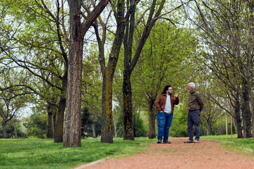 Obraz premium Intergenerational Conversation in a Public Park Between Two Men Walking on a Tree-Lined Path