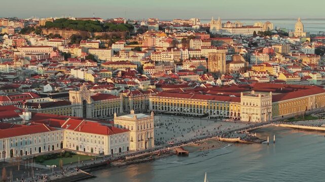 Aerial shot of Commerce Square and the Tagus River in Lisbon, Portugal at sunset. Red roofs and yellow buildings fill the historic center of Lisbon, Portugal