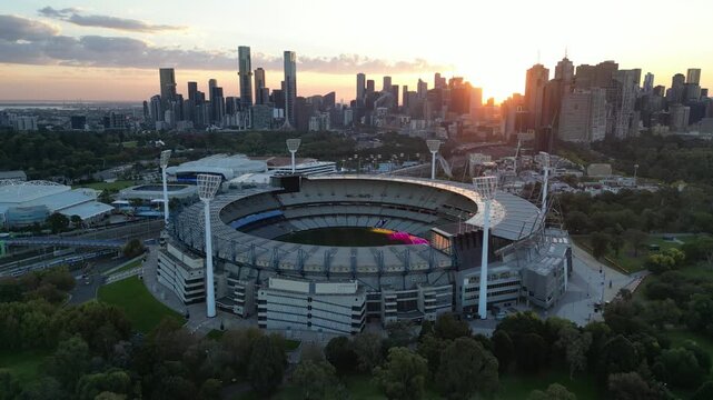 An aerial view of the Melbourne Cricket Ground (MCG) at sunset in front of the Melbourne City Skyline