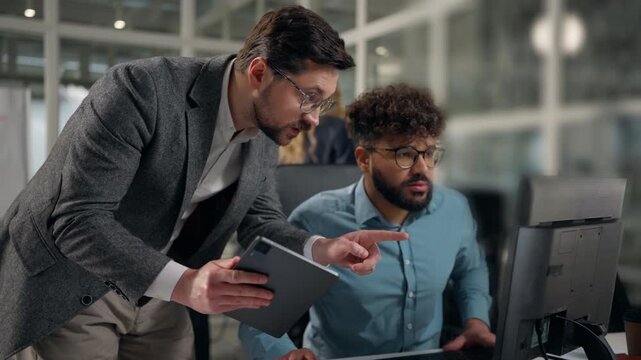 Two multiethnic business colleagues men businessmen talking comparing data in digital tablet compare information in laptop diversity men talk together analysing work multiracial partners in office