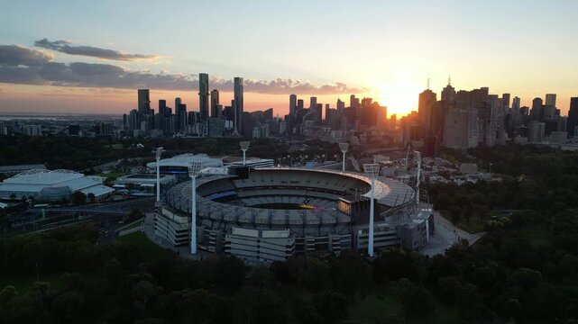 An aerial view of the Melbourne Cricket Ground (MCG) at sunset in front of the Melbourne City Skyline