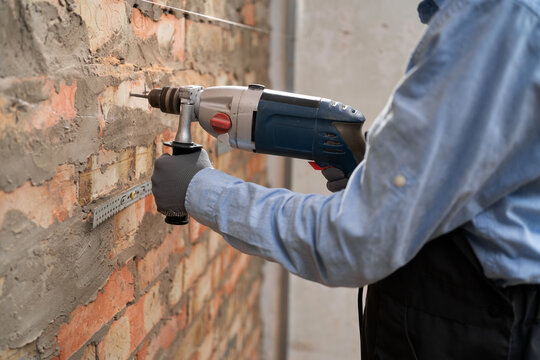 Builder worker with pneumatic hammer drill perforator making hole in wall working on construction site