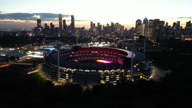 An aerial view of the Melbourne Cricket Ground (MCG) at sunset in front of the Melbourne City Skyline