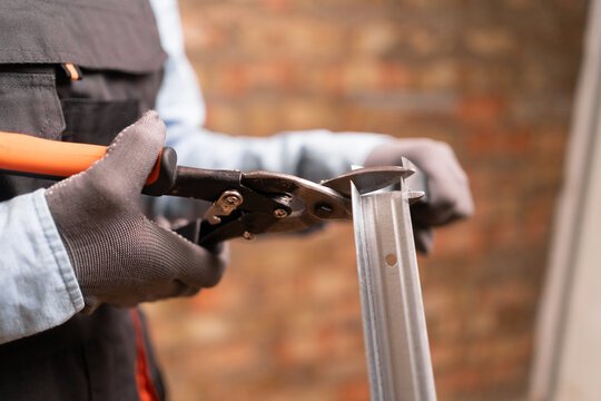 Construction worker using metal shears snips cut of galvanized steel from drywall profile.