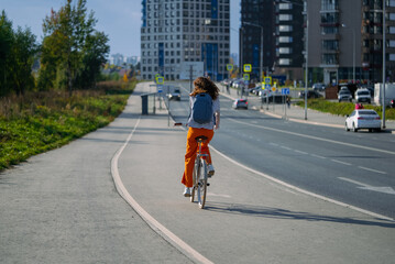 Naklejka premium Young woman enjoying active healthy lifestyle, riding bicycle on dedicated bike path in modern city, promoting sustainable urban transportation and eco-friendly commute