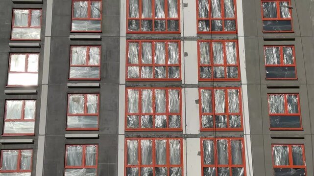 Apartment building under construction. block of flats with orange window frames and plastic bags instead of glass windows on wind weather.