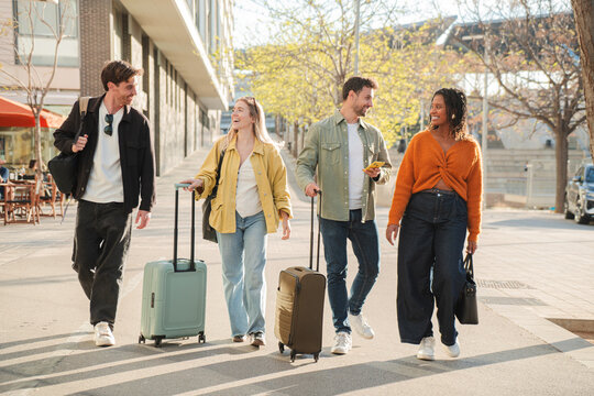 A lively group of friends strolls happily together, each pulling their colorful suitcases and enjoying their time as they embark on a new adventure filled with excitement and joy.